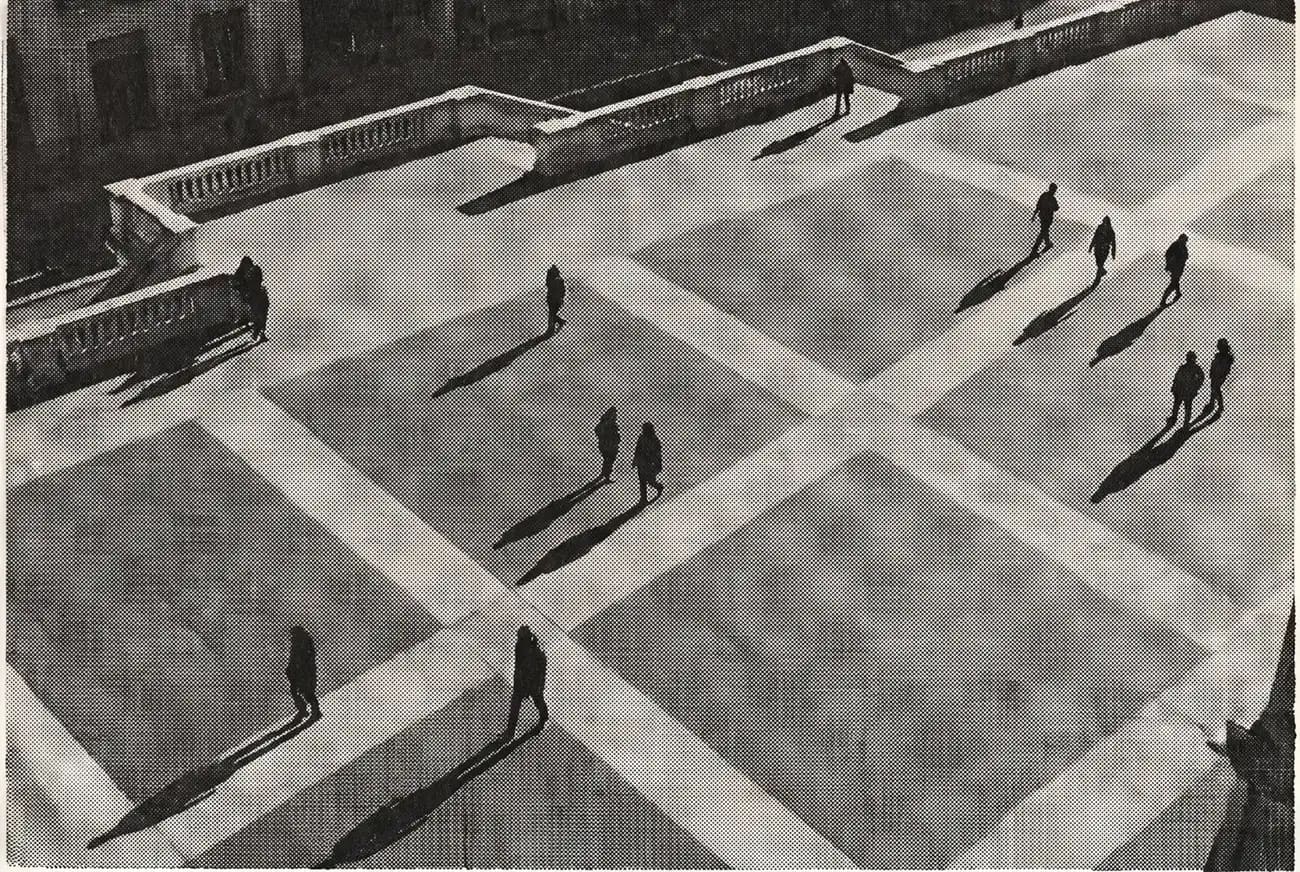 Una piazza pavimentata vista dall’alto, attraversata da figure minute