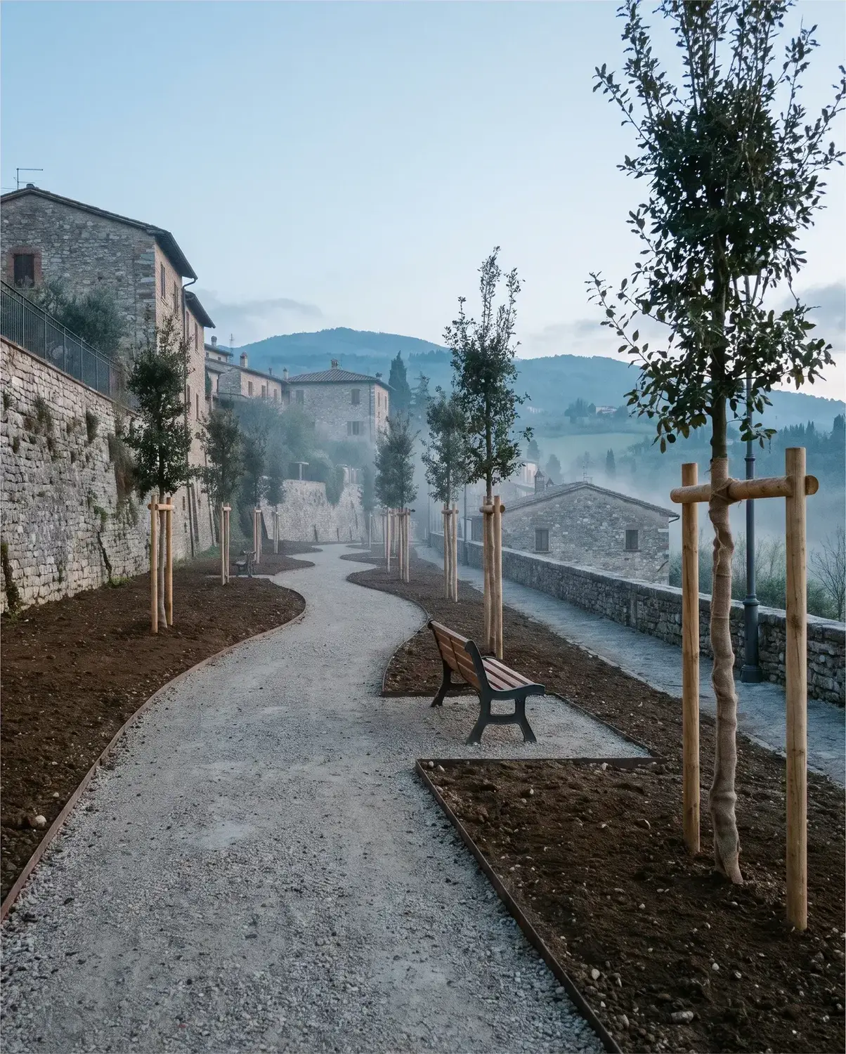 Un vialetto di parco appena risistemato, con alberi giovani e una panchina